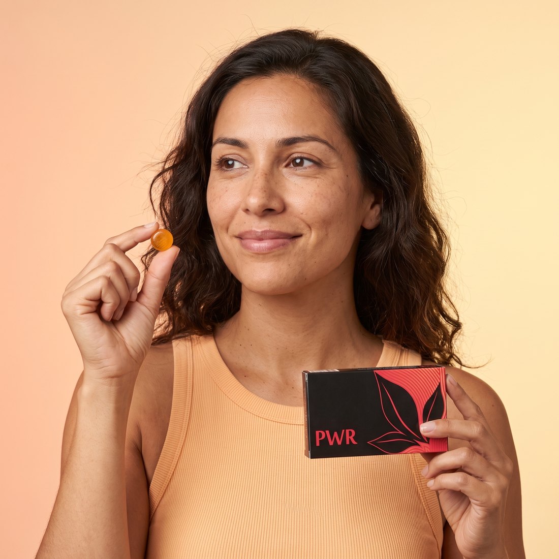 Mujer sonriente con una caja de PWR y una pastilla en la mano
