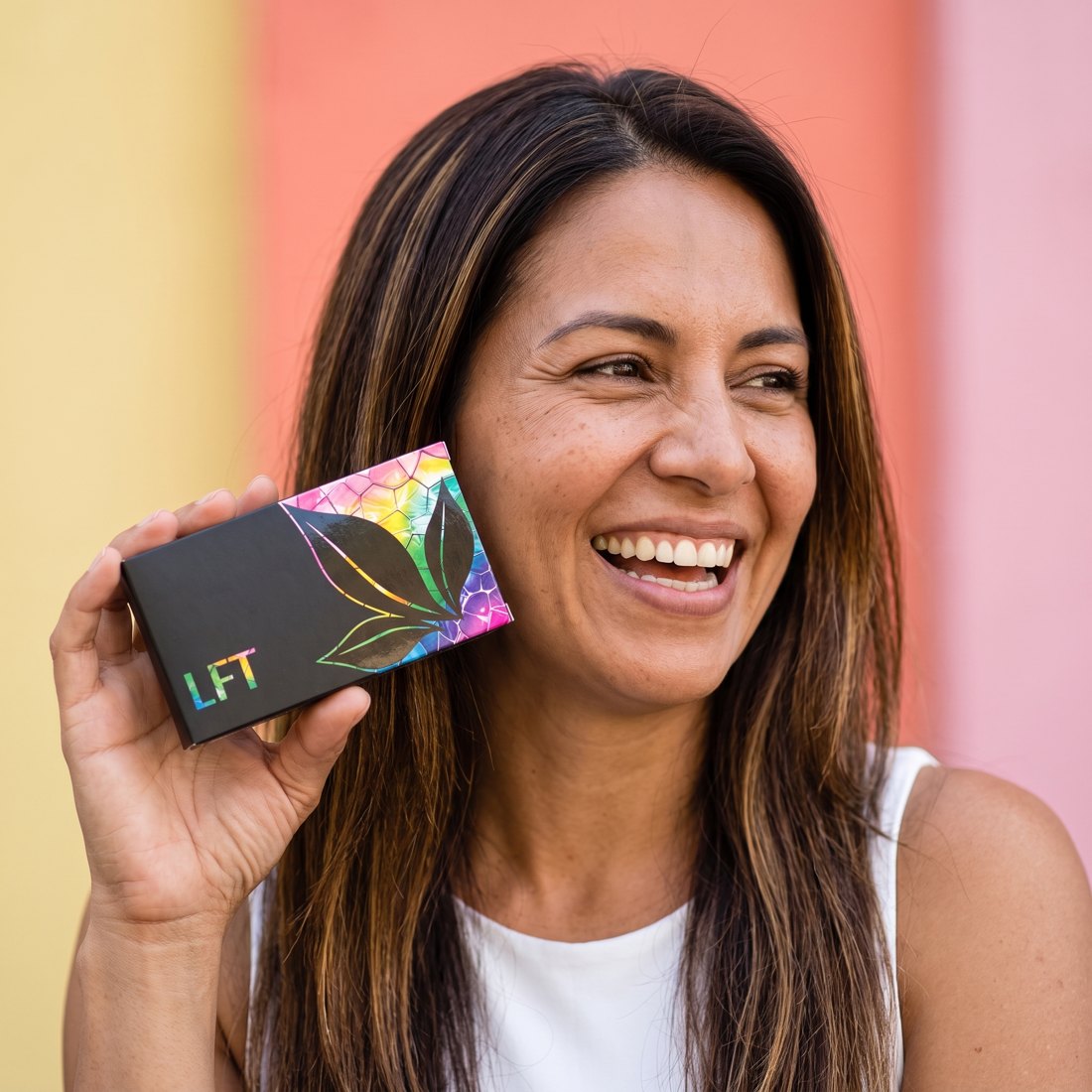 Mujer de pelo largo riendo con una caja de LFT junto a la cara